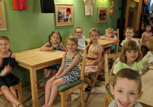 Zdjęcie przedstawia uśmiechnięte dzieci z grupy V siedzące na widowni w Baśniowej Kawiarence, czekające na rozpoczęcie przedstawienia
